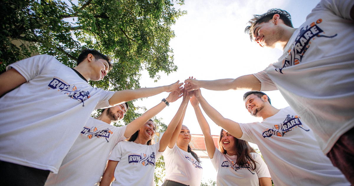 Diverse team standing in a circle outdoors with hands joined together, symbolizing teamwork and collaboration